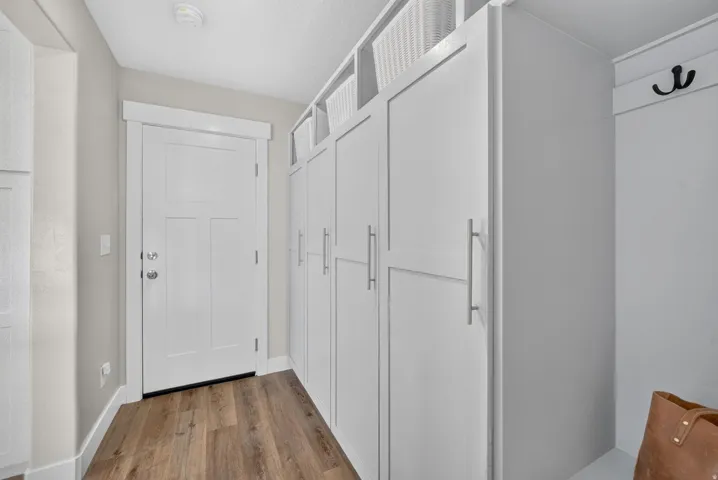 Entryway featuring wood-finish flooring, white paneled door, and built-in white cabinetry with brushed nickel hardware