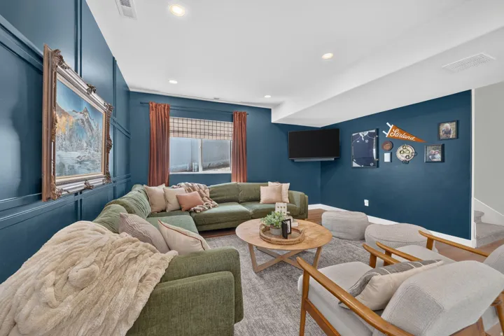 Recessed lighting, wood-finish flooring, accent wall paneling, wall-mounted television, and a window with blinds