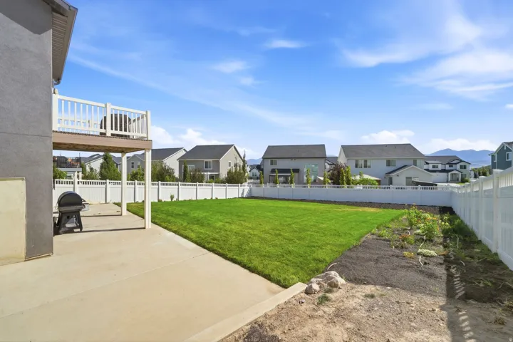 Expansive backyard with a manicured lawn, concrete patio, and a second-story balcony