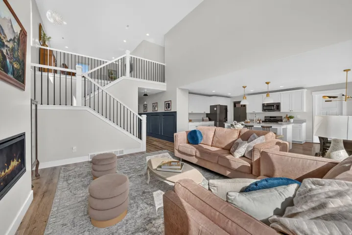 Open-concept living space with wood-finish flooring, a contemporary fireplace, and a multi-level staircase with white risers and black railings