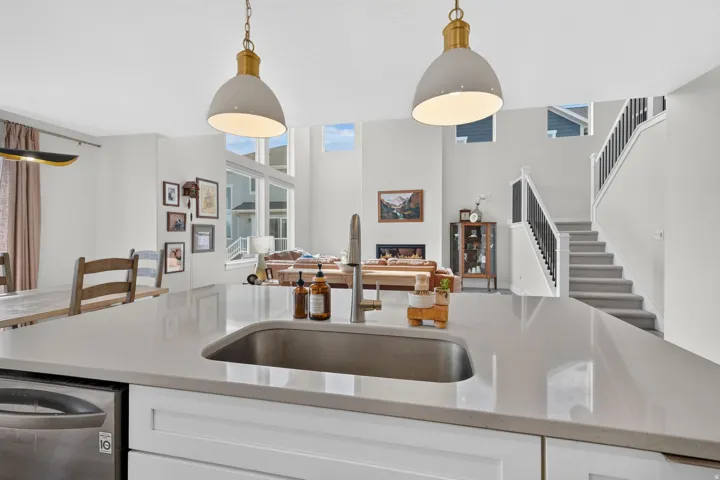 Waterfall edge island with integrated sink and stainless steel faucet, white shaker cabinetry, recessed lighting, and a high ceiling