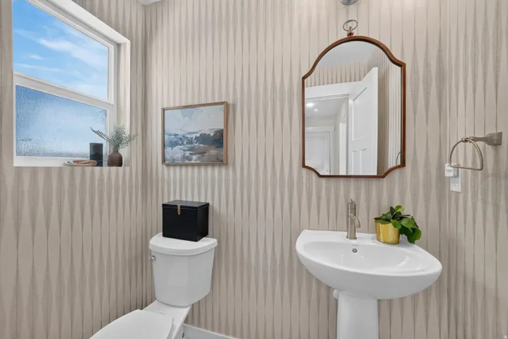 Pedestal sink with a single-handle faucet, wall-mounted mirror, and patterned wallpaper