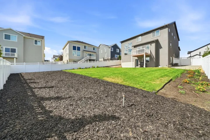Expansive backyard featuring a manicured lawn, a mulched area, and a white privacy fence