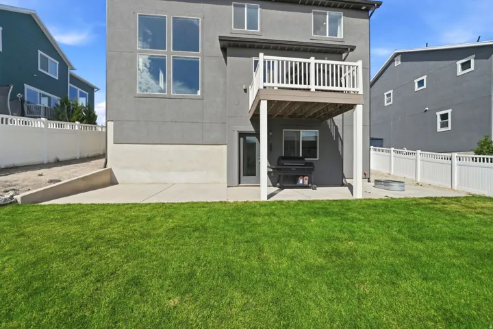 Expansive green lawn with a lower-level concrete patio, a second-story balcony, and white picket fencing enclosing the property perimeter
