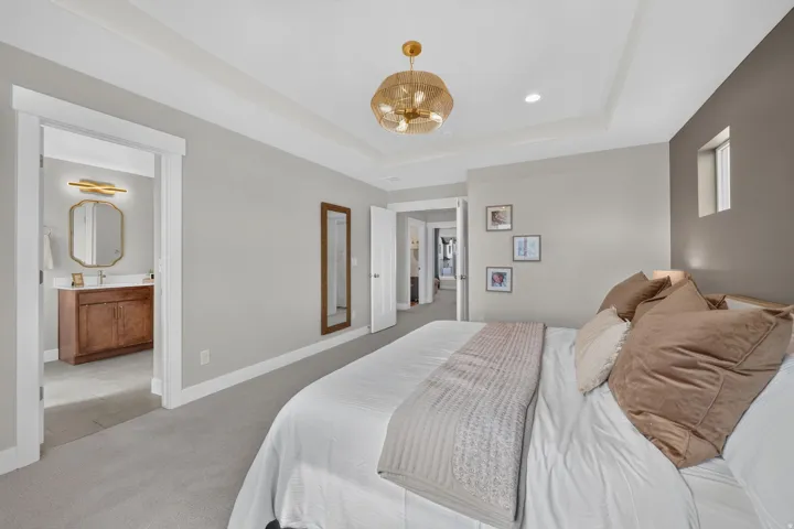Tray ceiling with a gold-toned chandelier, recessed lighting, and soft gray carpeting
