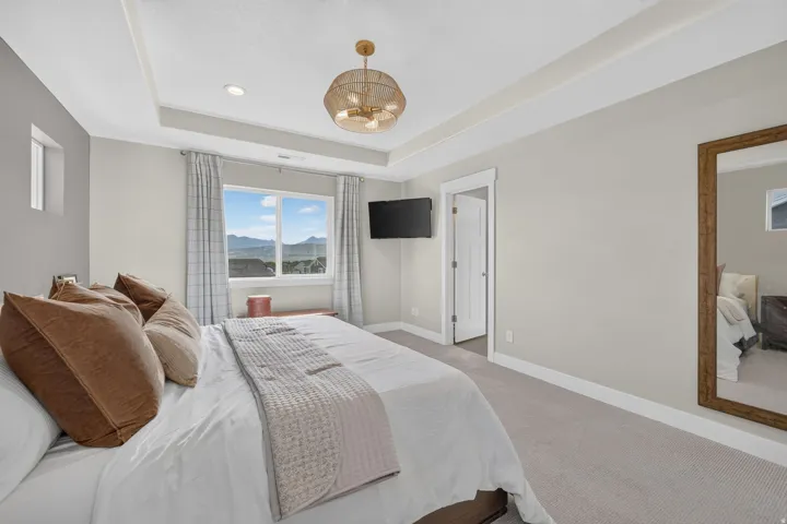 Tray ceiling with recessed lighting, woven pendant light fixture, window with exterior mountain scenery, wall-mounted television, and light-toned carpet