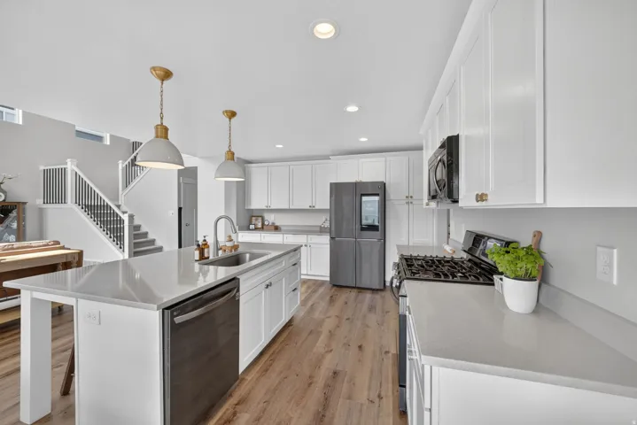 Kitchen featuring an expansive island with an integrated sink, white cabinetry, integrated stainless steel appliances, and wood-finish flooring