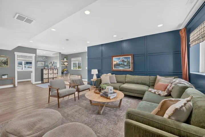 Wood-finish flooring, recessed lighting, accent wall with decorative paneling, large windows with blinds, and white trim throughout