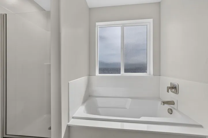 Soaking tub with brushed nickel fixtures, a frosted window, and a separate glass-enclosed shower