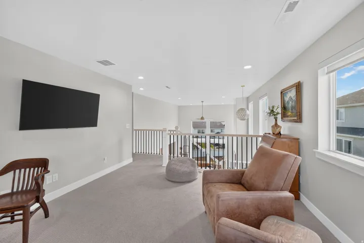 Carpeted loft area featuring a mounted television, recessed lighting, and a black metal railing overlooking a lower level