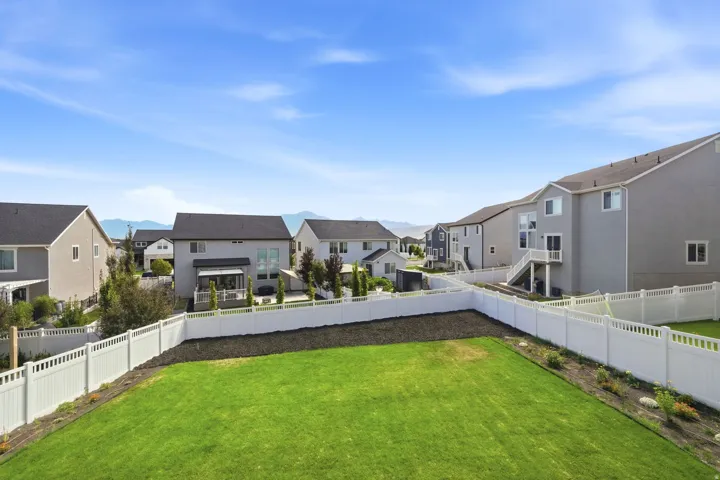 Expansive backyard featuring a manicured lawn, established landscaping, and a white privacy fence
