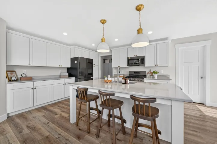 White shaker cabinetry, wood-finish flooring, white countertops, built-in stainless steel appliances, and a central island with pendant lighting