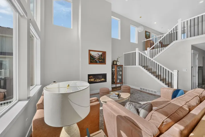 Two-story living area with high ceilings, large windows, a built-in fireplace, and a multi-level staircase with white and black railings