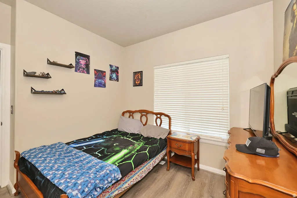 Wood-finish flooring with neutral wall paint, a window with horizontal blinds, and a built-in wall shelf system