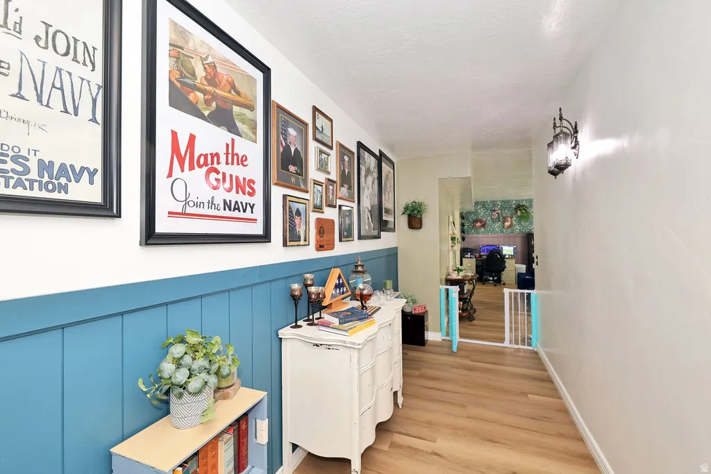 Hallway with wood-finish flooring, half-wall wainscoting, and a decorative wall sconce