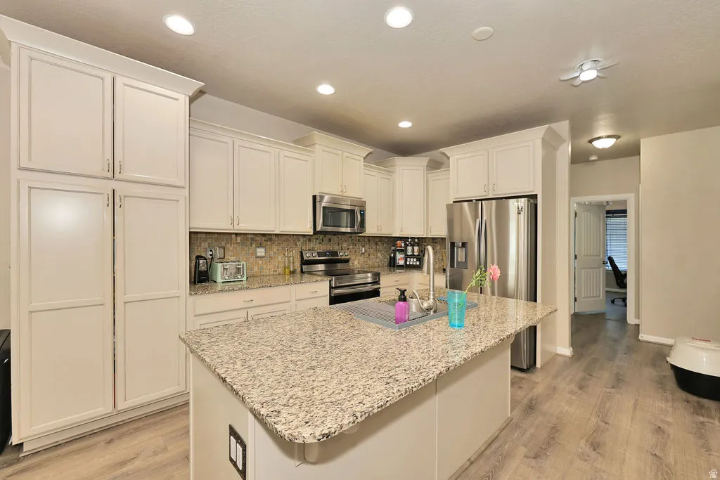 Central island with stone countertop, stainless steel appliances, wood-finish flooring, recessed lighting, and white cabinetry