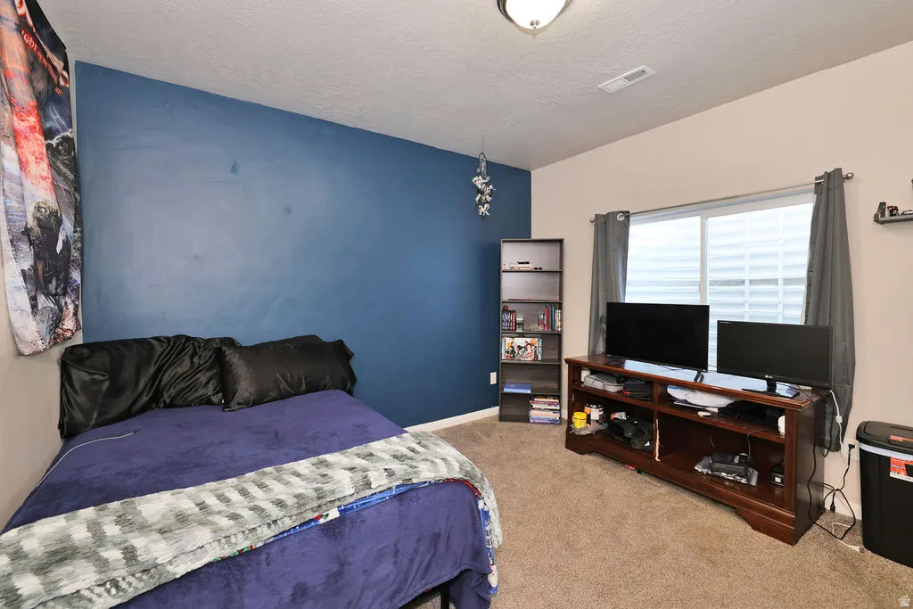Carpeted flooring, a window with horizontal blinds and draperies, a wall-mounted light fixture, and a built-in shelving unit