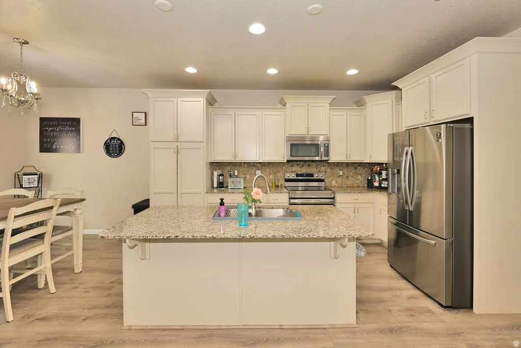 Kitchen featuring light-toned cabinetry, stainless steel appliances, a center island with a sink, and wood-finish flooring