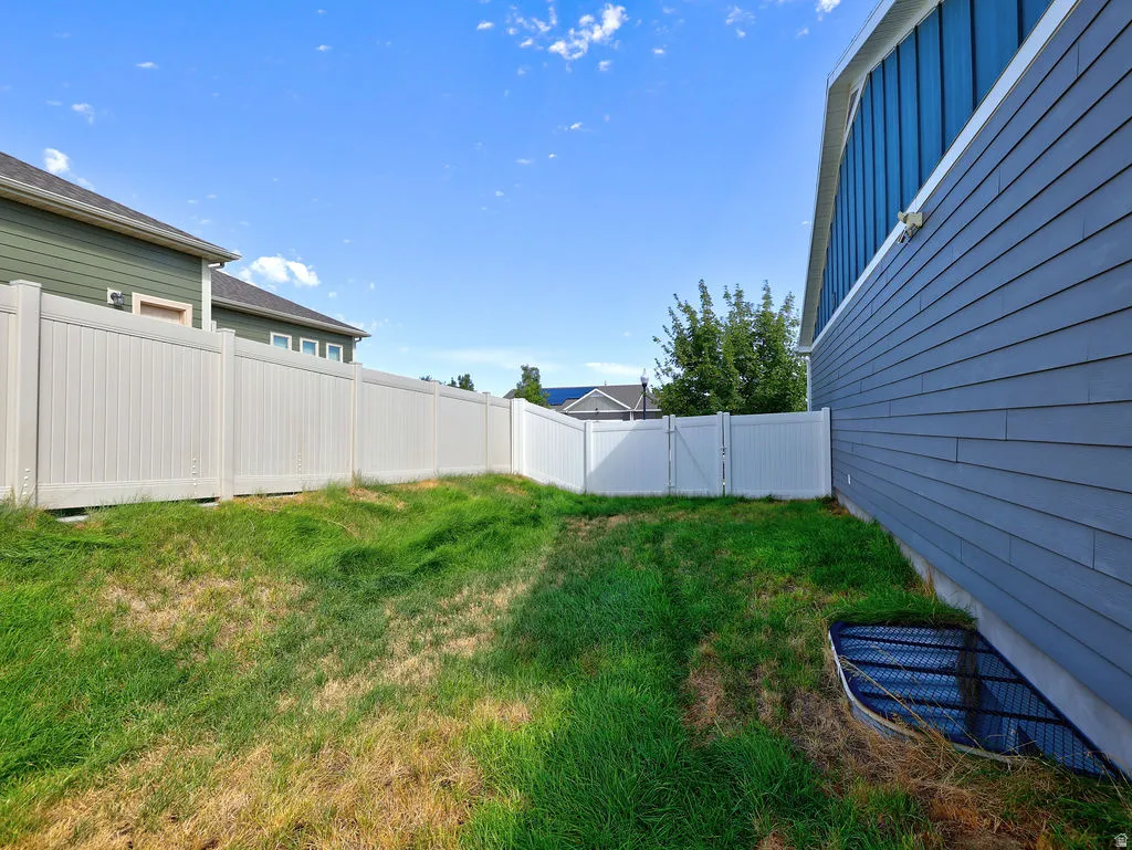 Fenced yard featuring a white privacy fence with a gate, blue horizontal siding, and a window well with a security grate