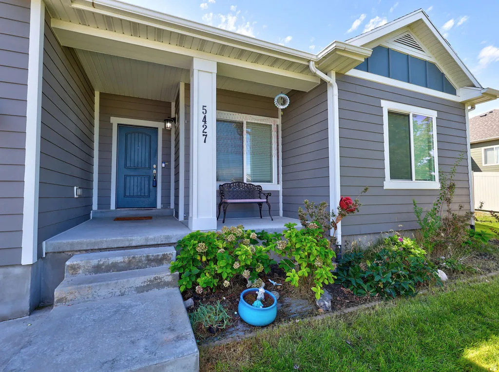 Gray horizontal siding with white trim, blue front door, covered concrete porch, and landscaped garden beds