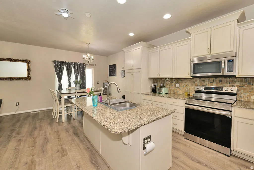 Kitchen featuring an island with a built-in sink, granite countertops, stainless steel appliances, and white cabinetry