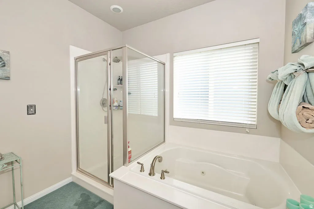 Frameless glass shower enclosure, built-in soaking tub, recessed lighting, and a large window with privacy blinds