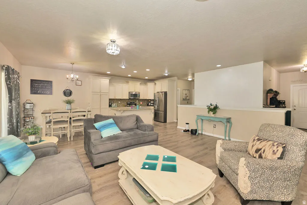 Open-concept living space featuring wood-finish flooring, recessed lighting, a crystal chandelier, and a breakfast bar with stone countertops
