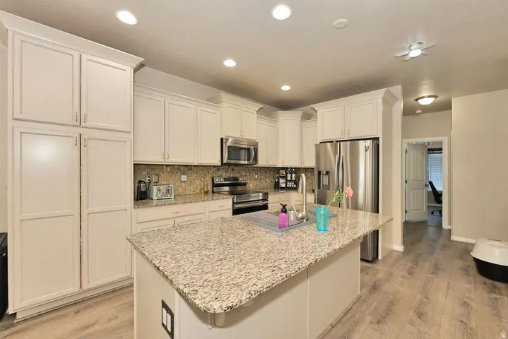 Central island with stone countertop, stainless steel appliances, wood-finish flooring, recessed lighting, and white cabinetry