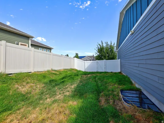 Fenced yard featuring a white privacy fence with a gate, blue horizontal siding, and a window well with a security grate
