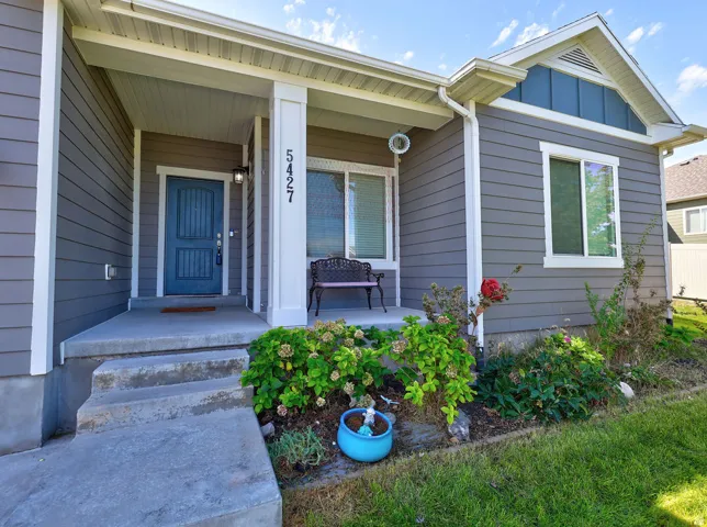 Gray horizontal siding with white trim, blue front door, covered concrete porch, and landscaped garden beds