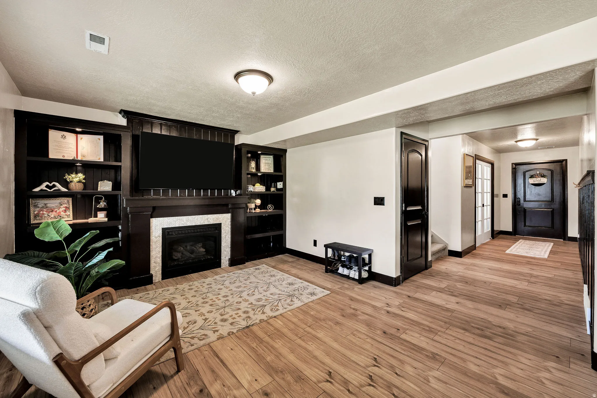 Hardwood-finish flooring throughout, dark wood built-in shelving, integrated fireplace with light-toned surround, dark-paneled interior doors, and a decorative front entry door