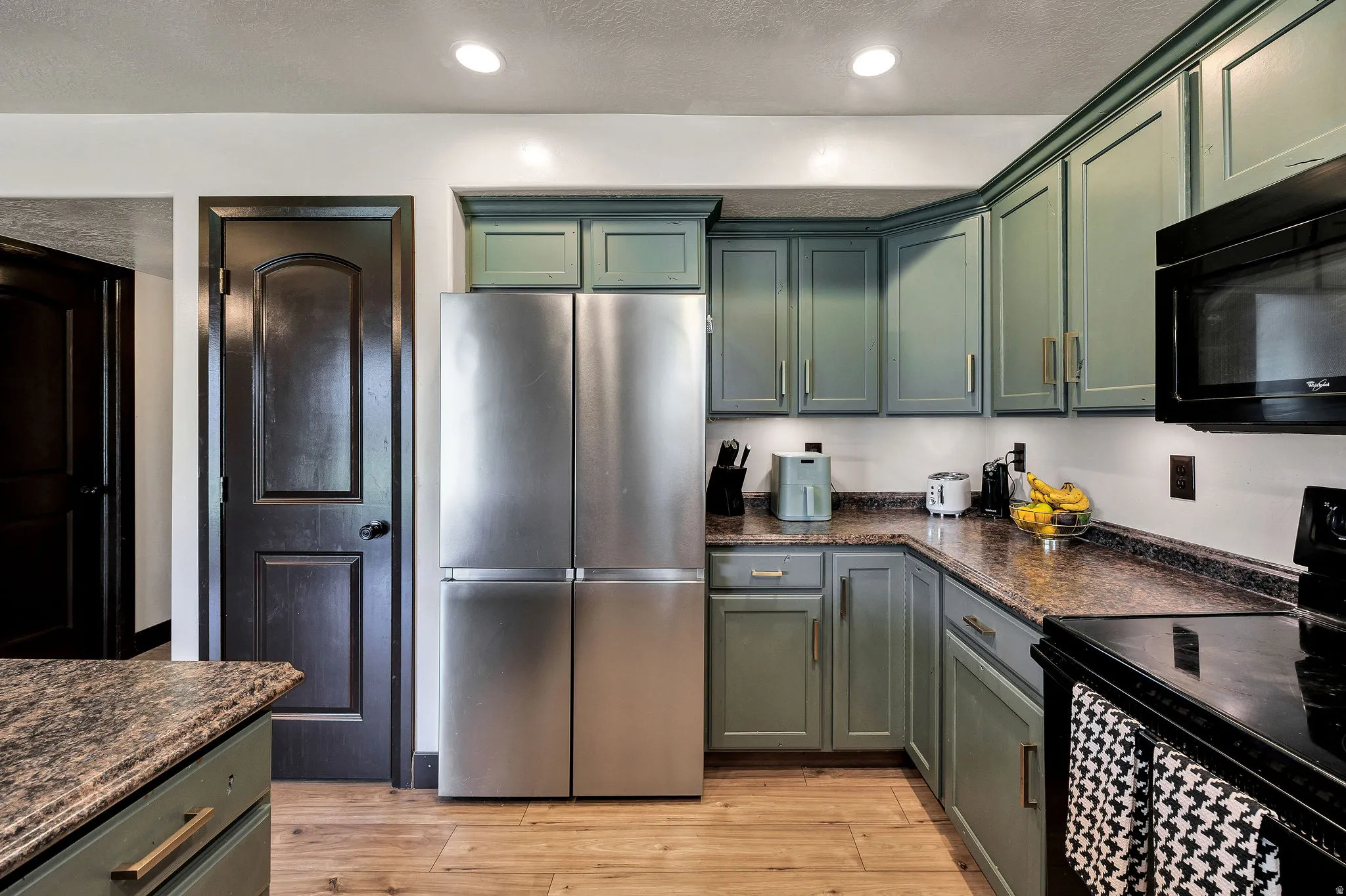 Kitchen featuring recessed lighting, stainless steel refrigerator, dark countertops, green cabinetry with gold-tone hardware, and wood-finish flooring