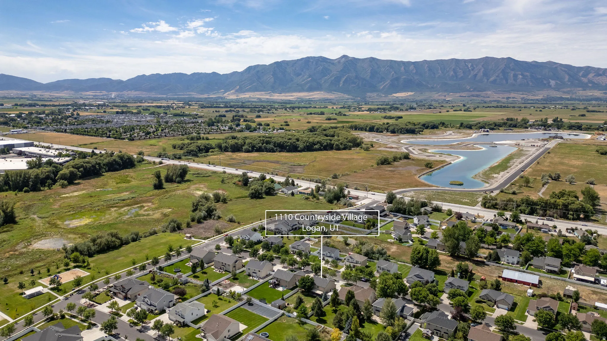 Aerial perspective of a residential community with established homes, surrounded by expansive green spaces and mountainous terrain