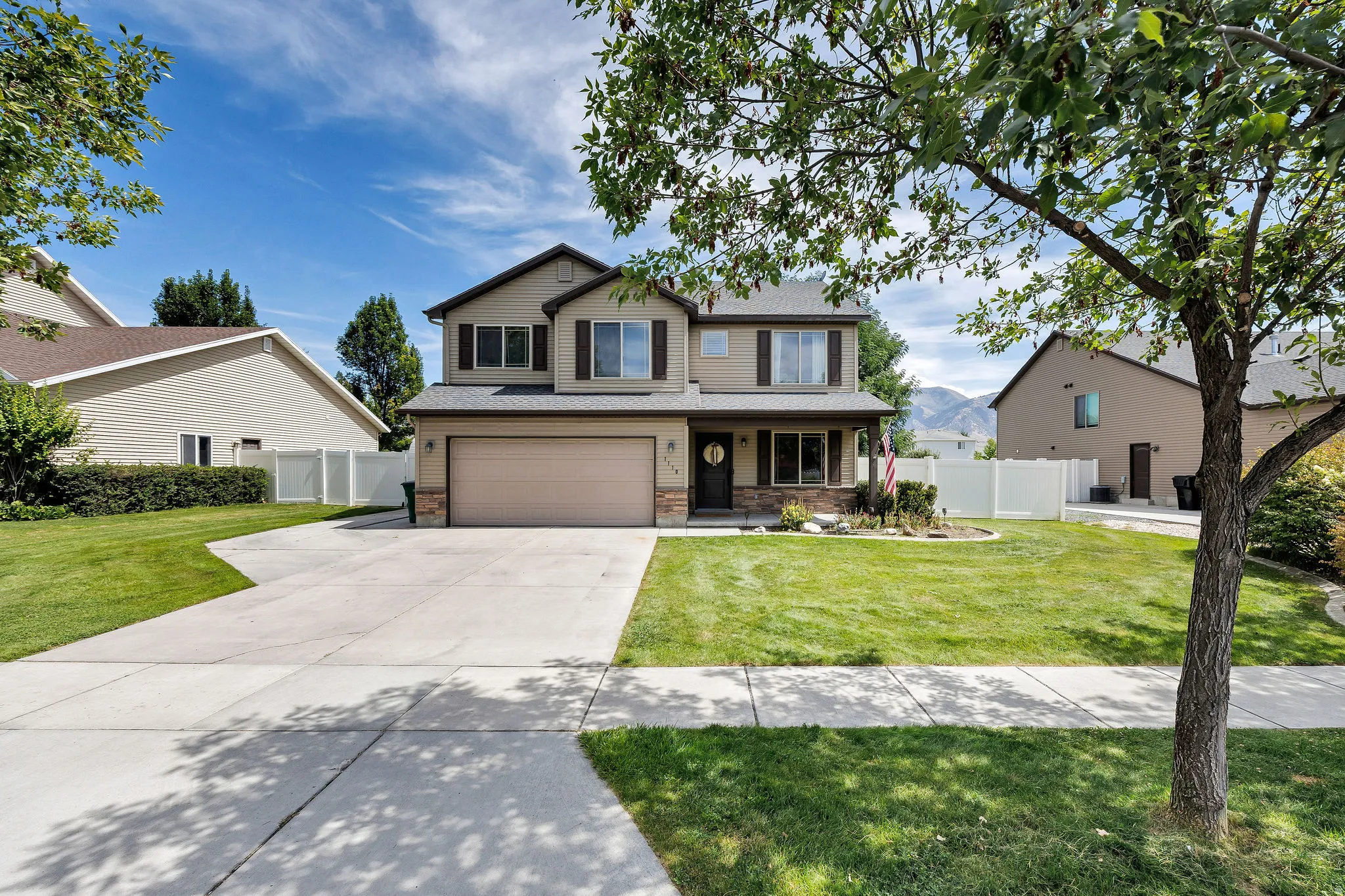 Two-story residence featuring a two-car garage, stone accents, and a landscaped front yard with a concrete driveway