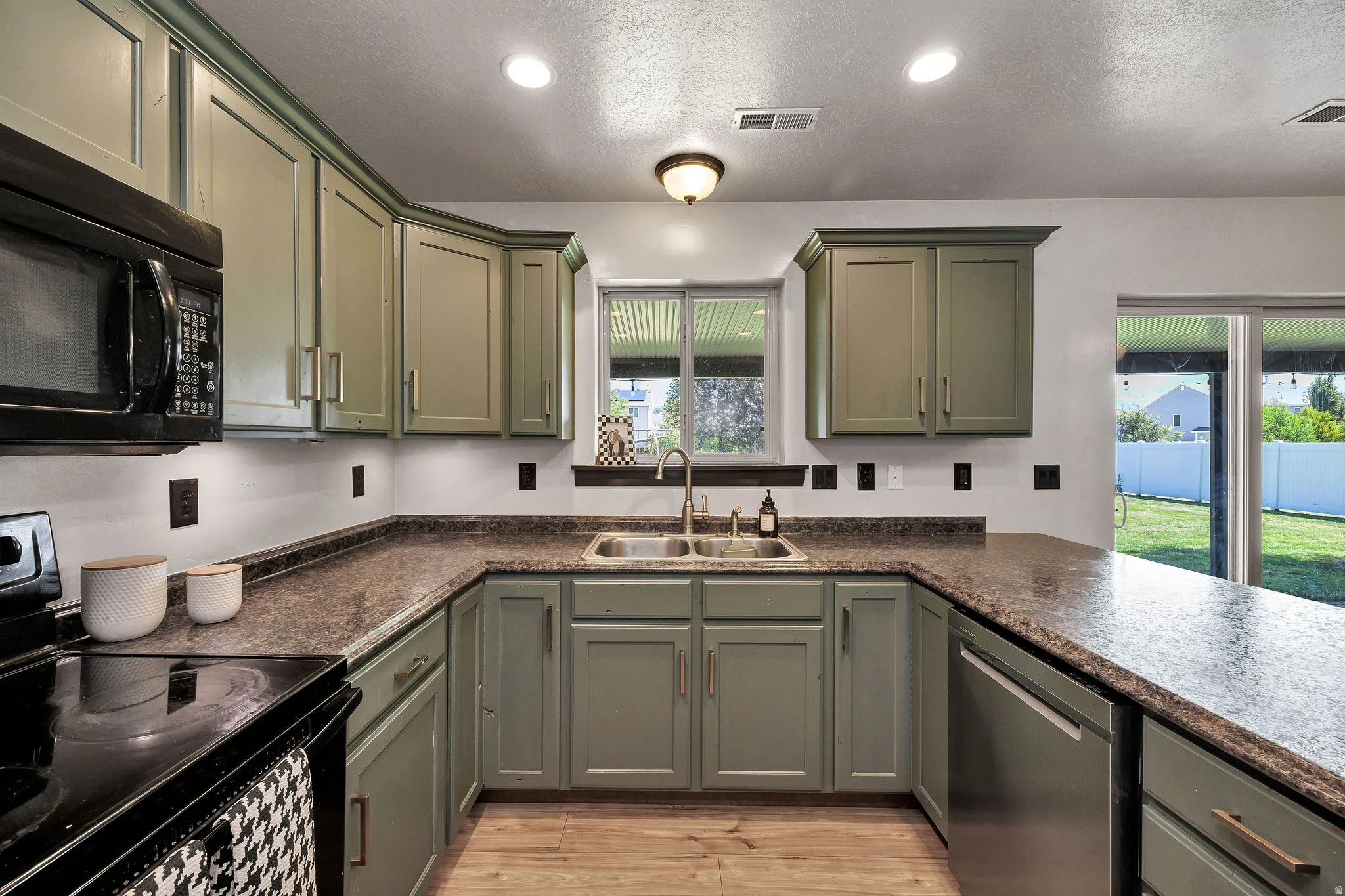U-shaped kitchen featuring wood-finish flooring, recessed lighting, green cabinetry, dark countertops, and stainless steel appliances