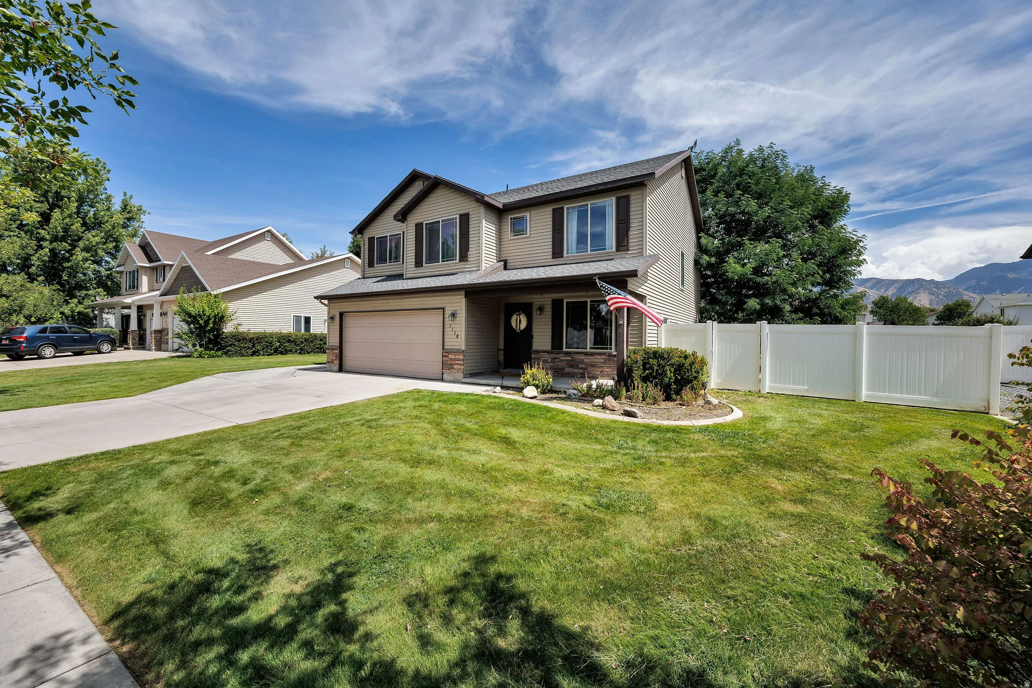 Two-story residence with a two-car garage, stone and siding exterior, and a white vinyl fence