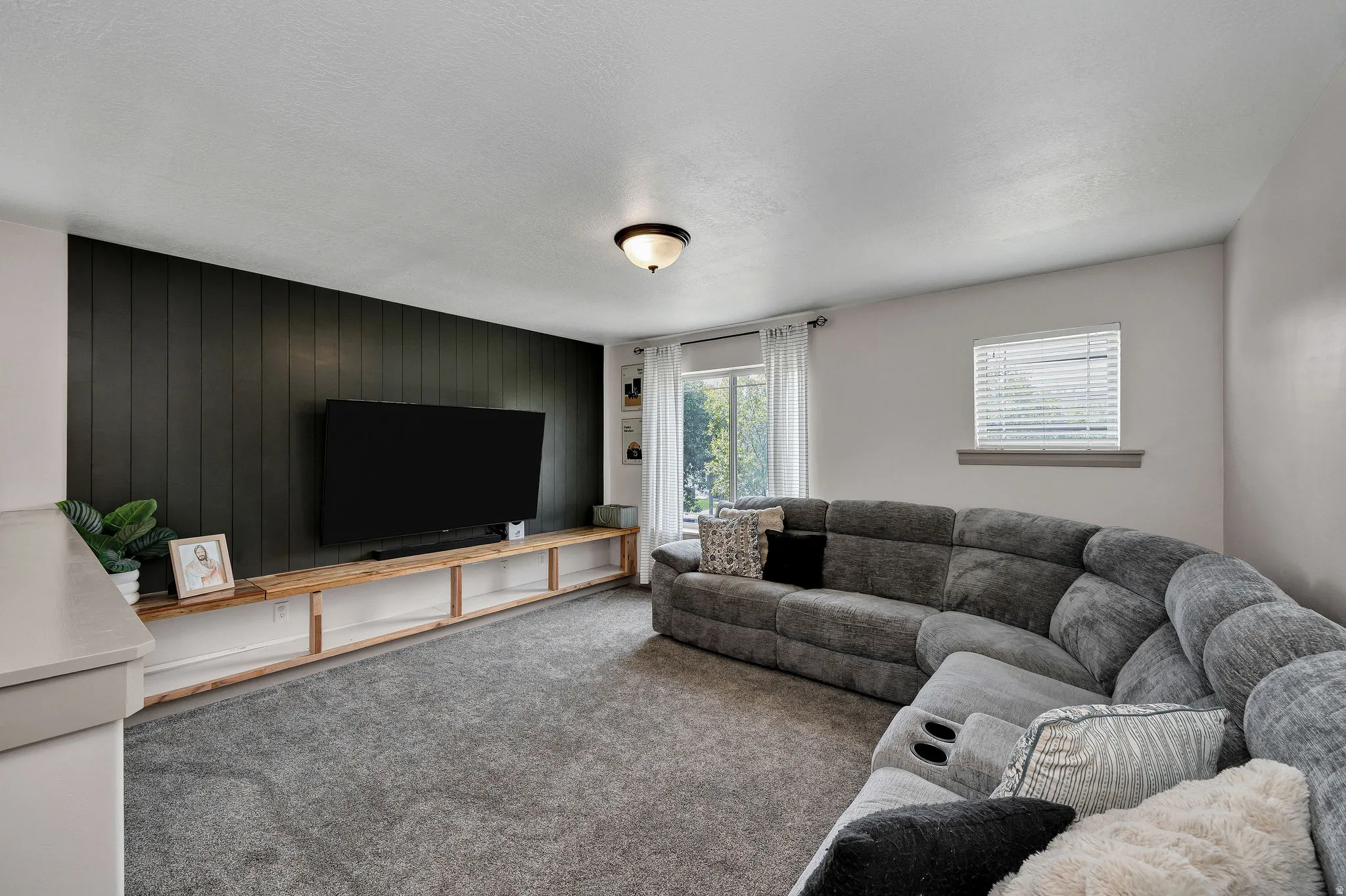 Accent wall with vertical paneling, wood-finish built-in shelving, windows with natural light, and ceiling-mounted light fixture