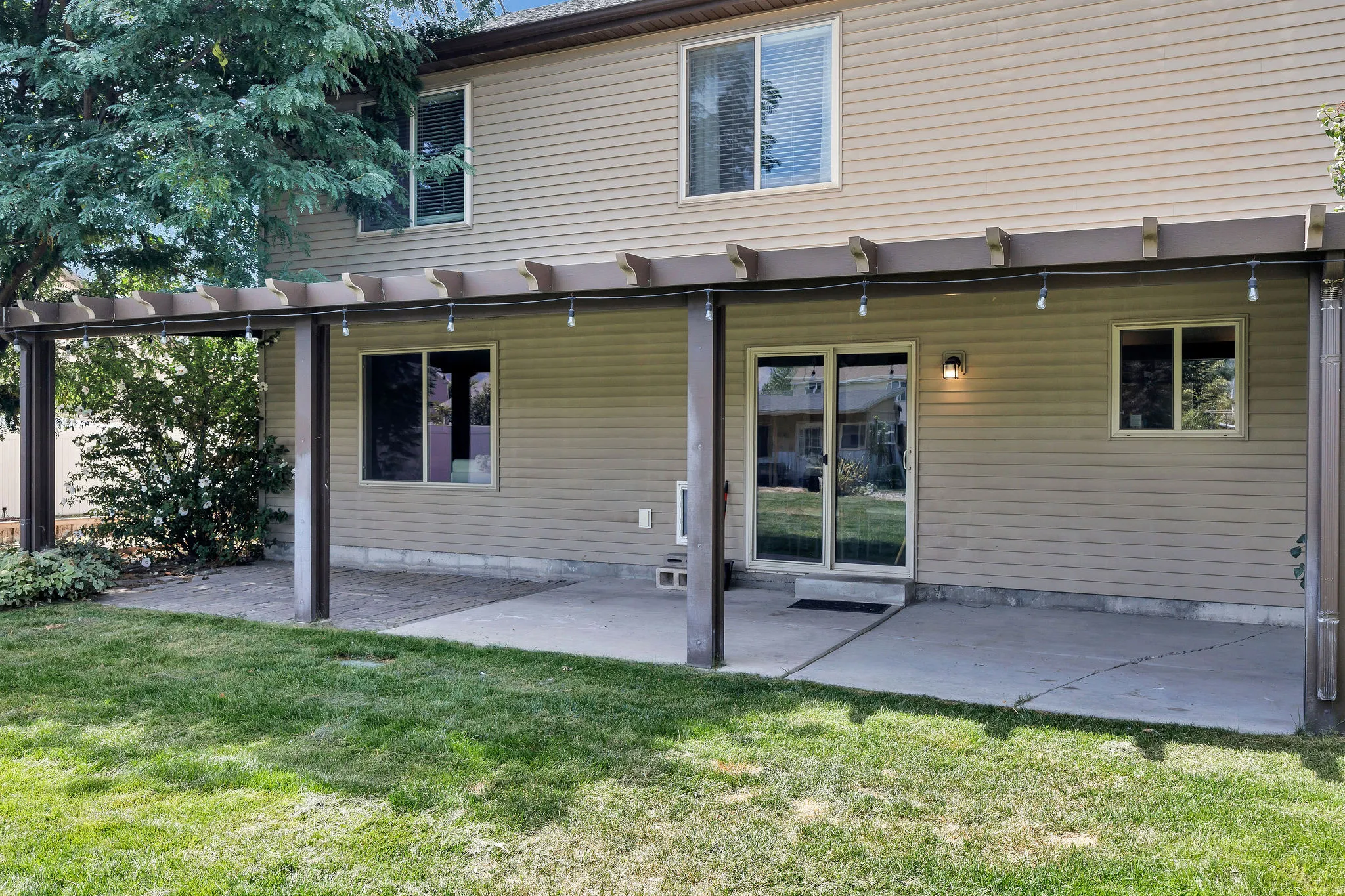 Attached pergola featuring string lighting over a concrete patio and paver patio