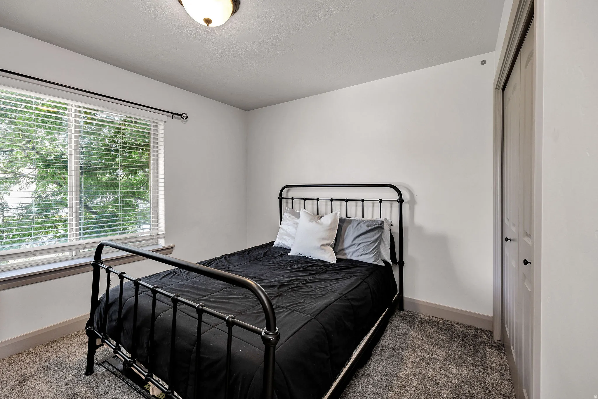 Wall-to-wall carpeting, window with horizontal blinds, built-in closet with bifold doors, and a ceiling-mounted light fixture