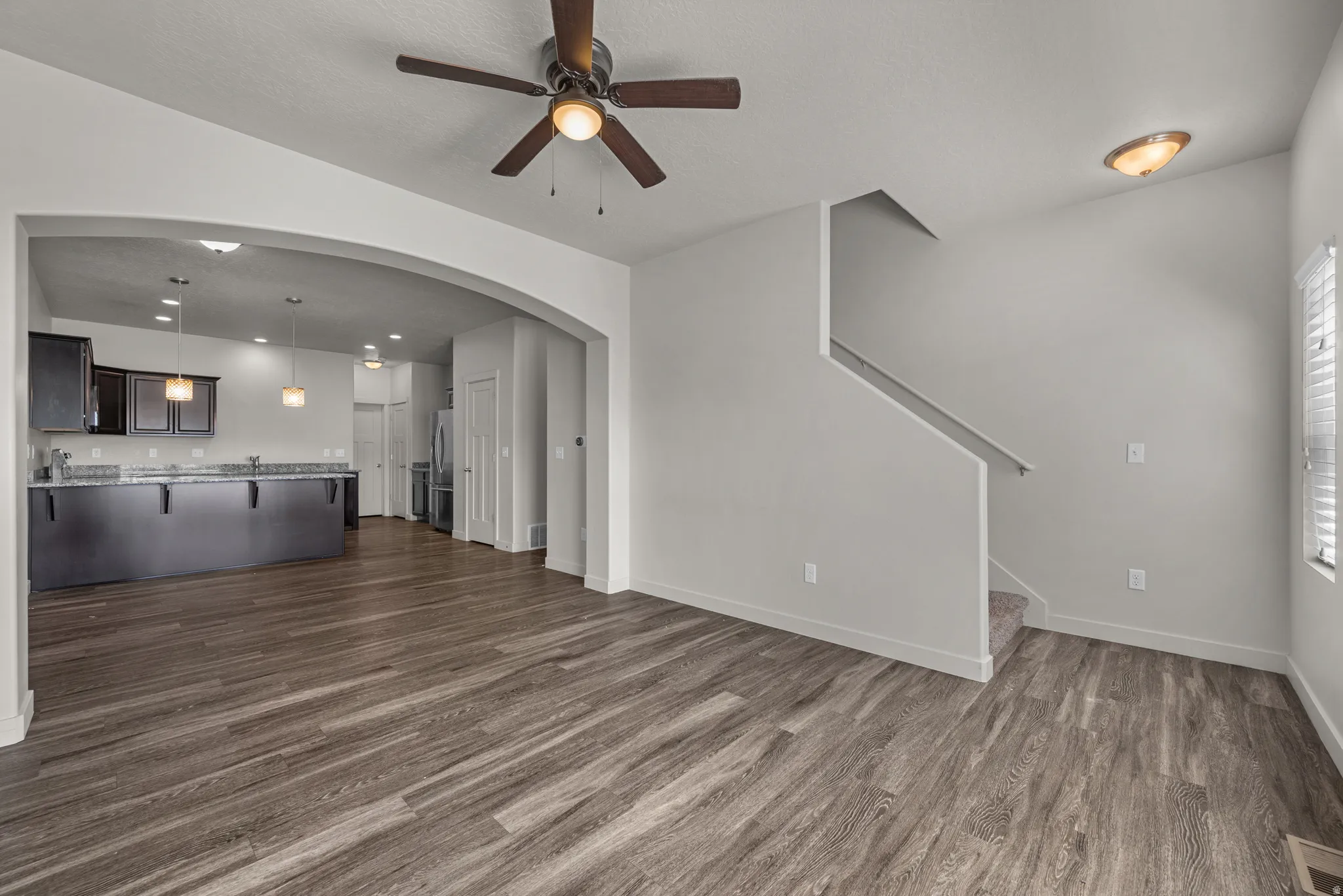 Expansive living area with wood-finish flooring, an arched entryway, and a ceiling fan