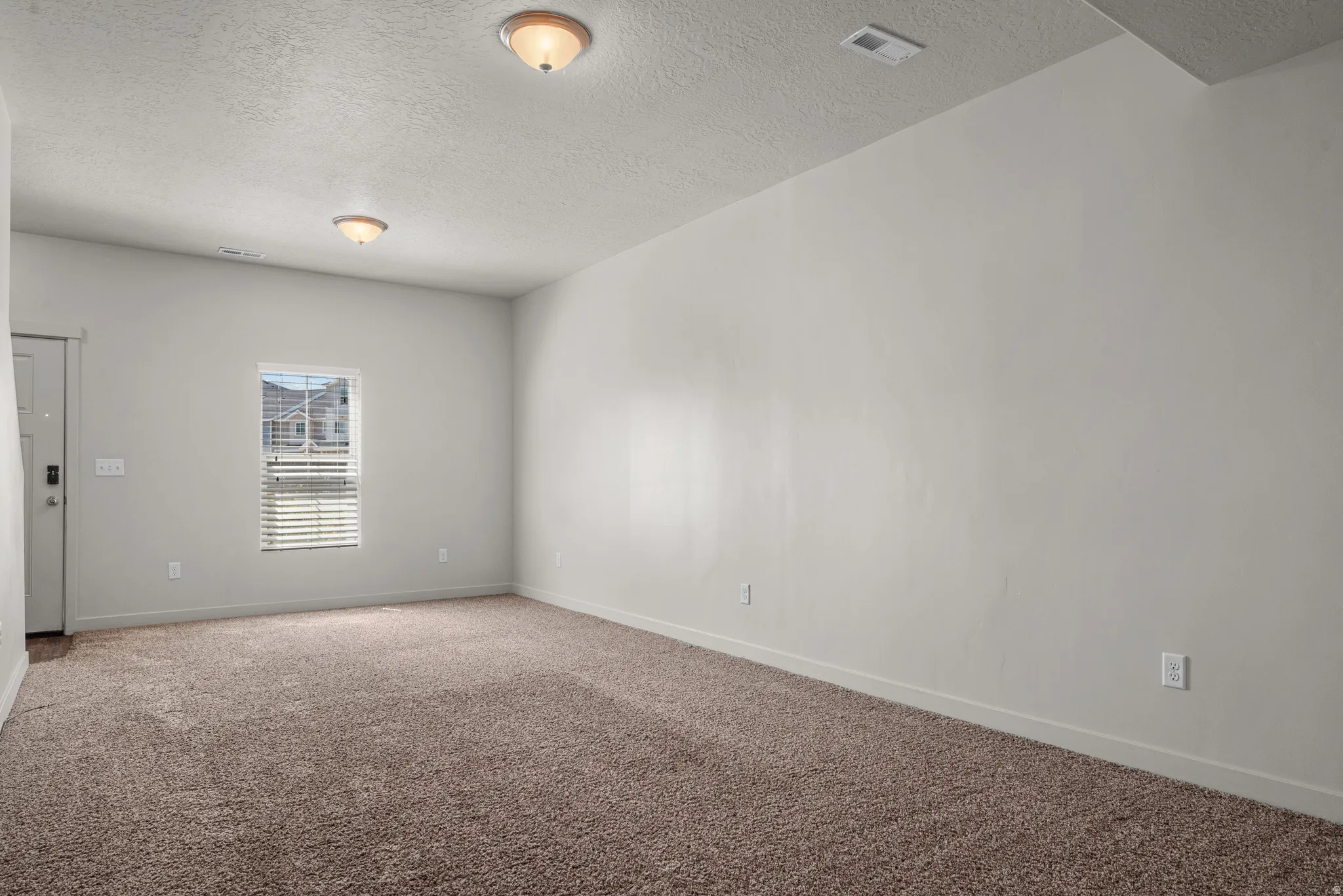 Spacious room featuring neutral carpeting, light-colored walls, and a window with blinds