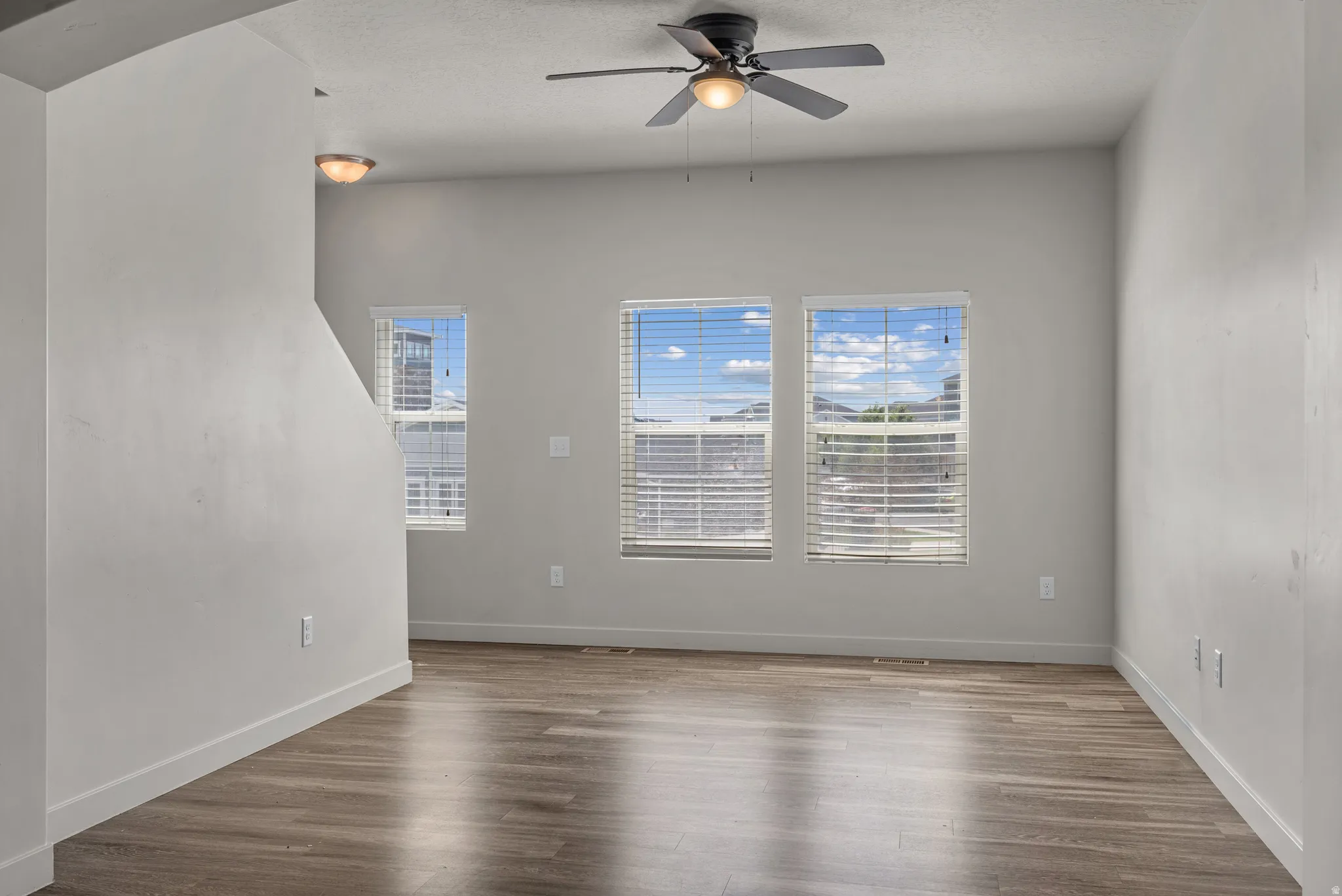 Wood-finish flooring, multiple windows with horizontal blinds, overhead ceiling fan with lighting, and recessed ceiling light fixtures