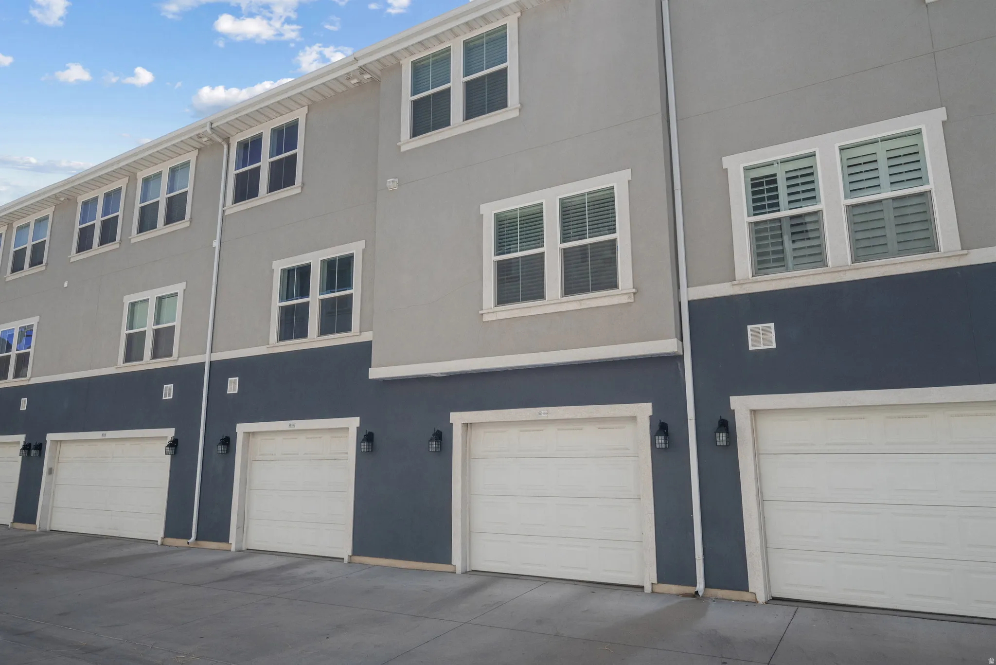 Multi-level exterior with a two-tone facade, white garage doors, and exterior wall sconces
