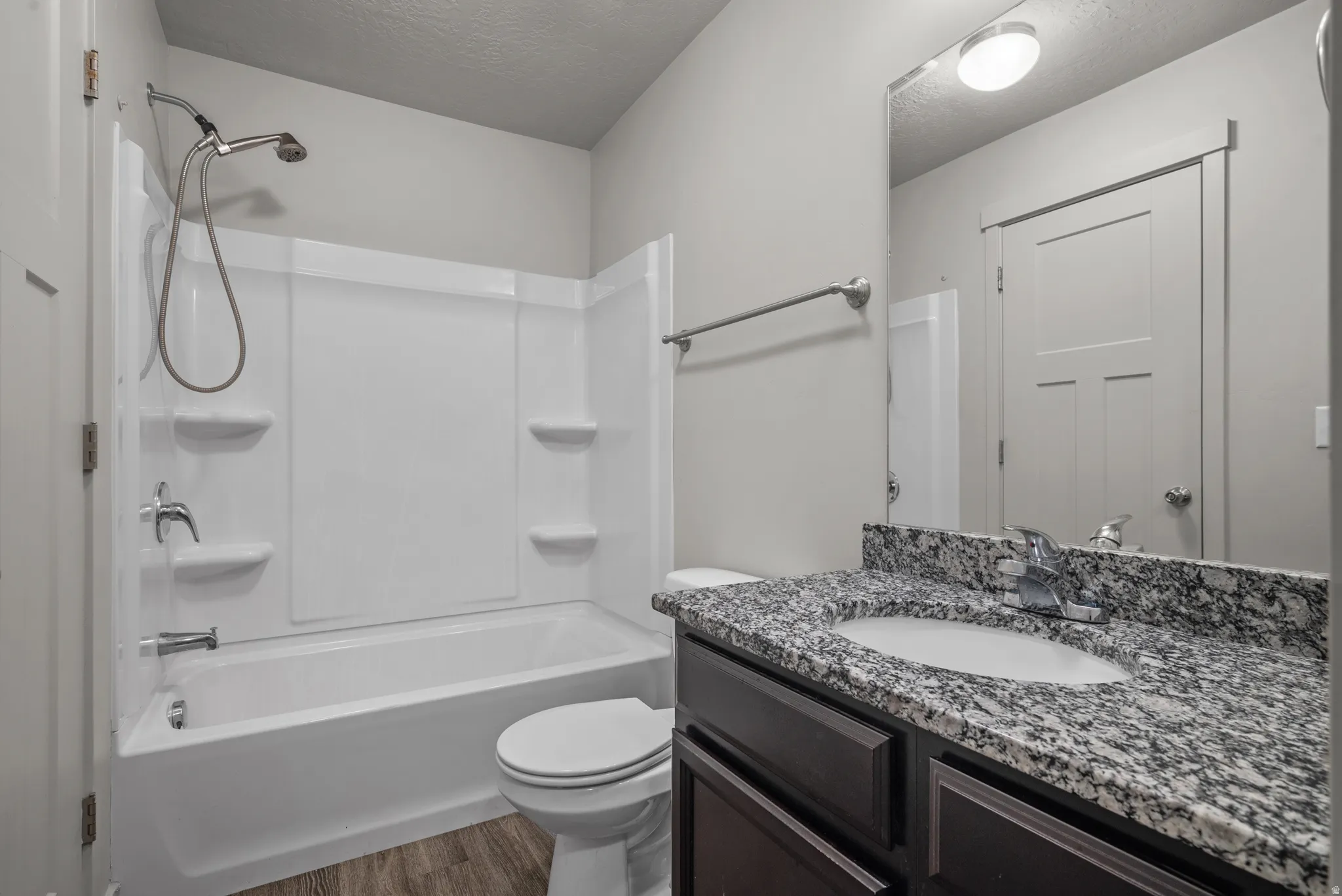 Bathroom featuring a shower/tub combination, vanity with a rectangular basin, granite countertop, and wood-finish flooring