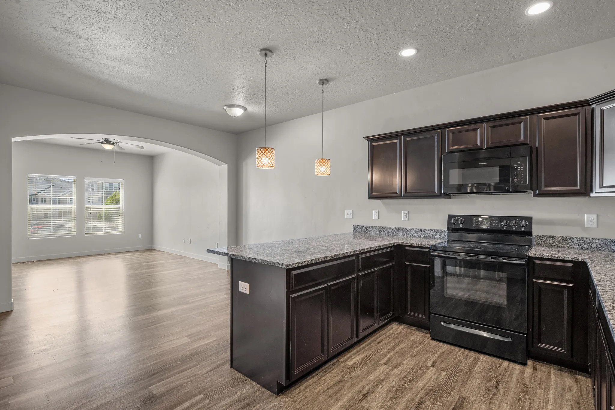Kitchen featuring dark wood-finish cabinetry, black appliances, and speckled countertops