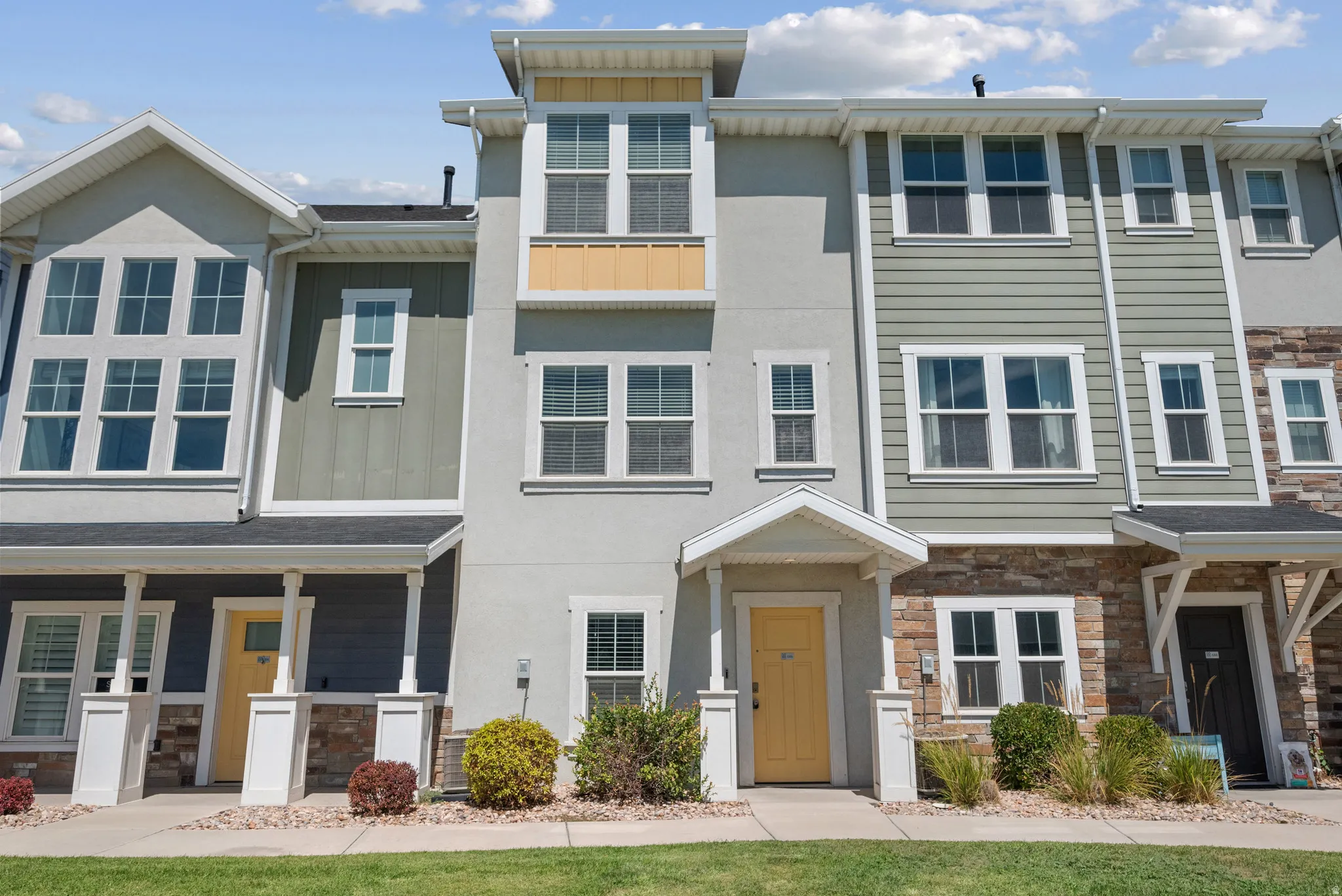 Multi-level townhouse facade featuring a covered entry, stucco and siding exterior, and a stone accent wall