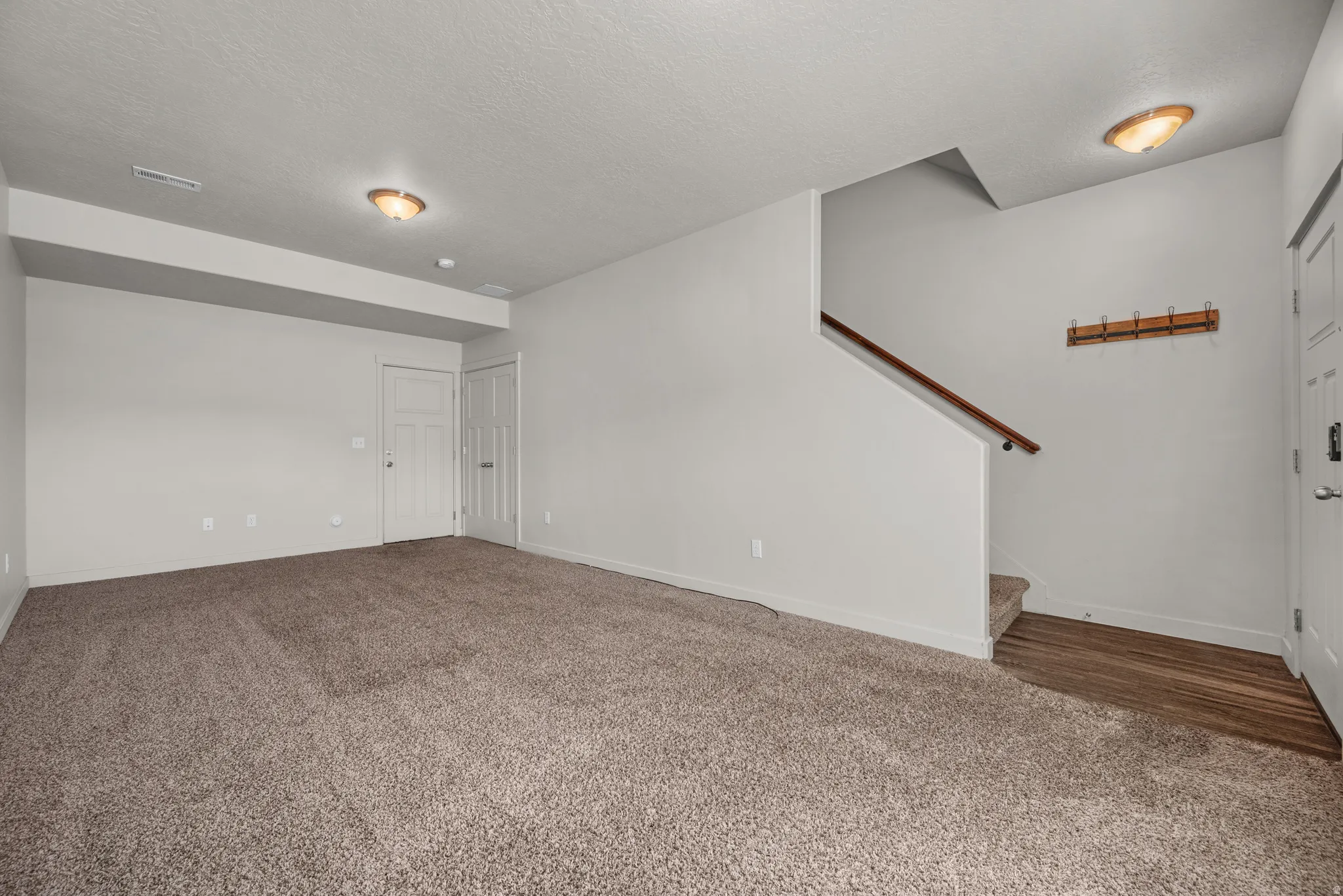 Open area with carpet flooring, a staircase with a wood handrail, and recessed lighting