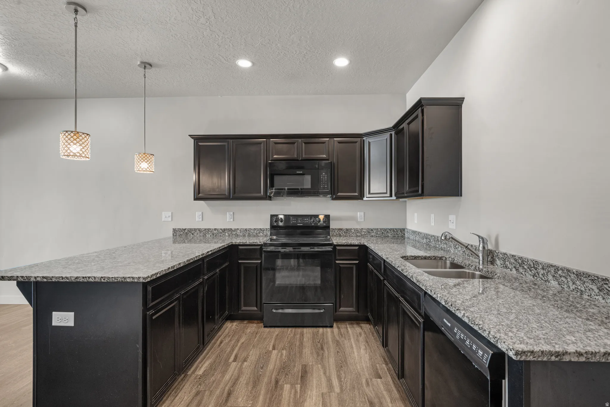 Kitchen featuring dark wood-finish cabinetry, light-toned countertops, a stainless steel double basin sink, and wood-finish flooring