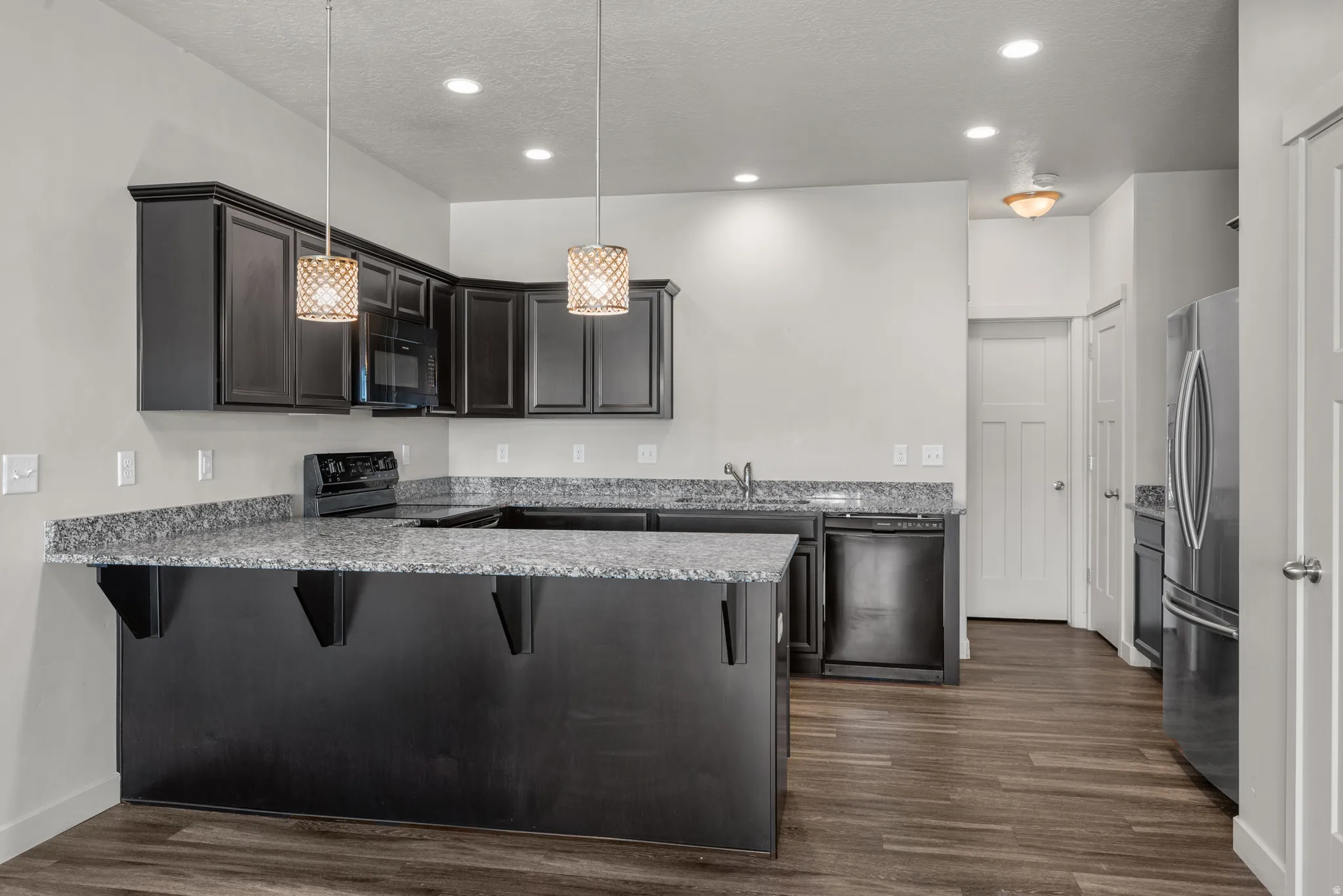 Kitchen featuring dark wood-finish cabinetry, granite-style countertops, stainless steel appliances, and wood-finish flooring