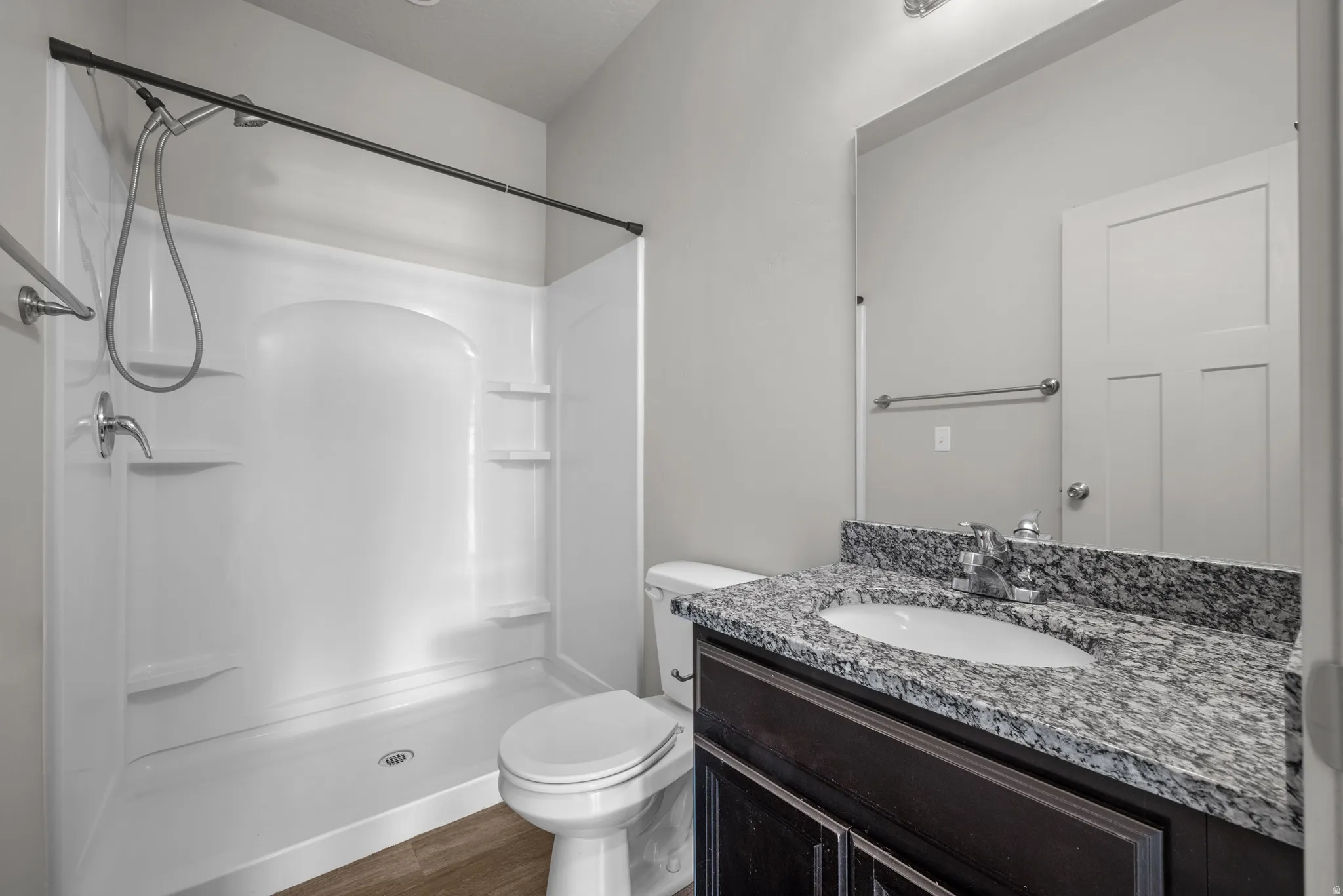 Granite countertop vanity with integrated sink, wood-finish flooring, and a white shower stall with built-in shelving